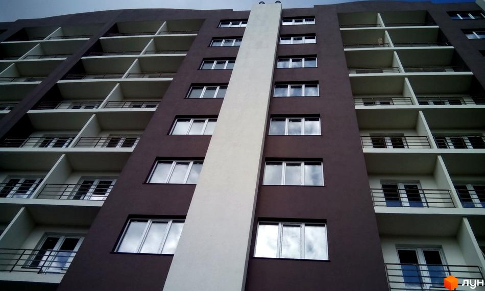 Фасад житлового комплексу Вишнева оселя з численними балконами та вікнами. Будинок має коричневий колір стін та білу вертикальну вставку.