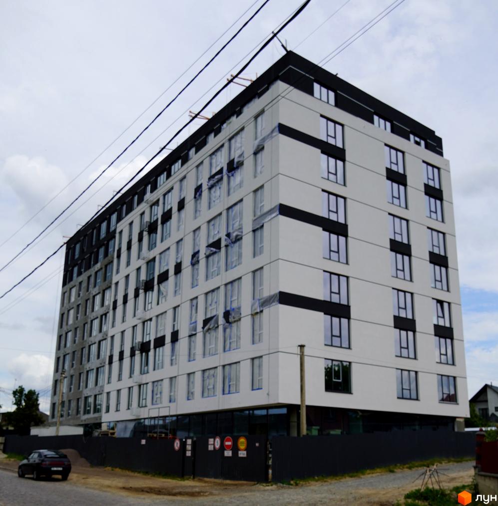 Зовнішній вигляд новобудови ЖК SVIY з біло-чорними фасадами та великою кількістю вікон. На прибудинковій території видно паркан та дорогу.