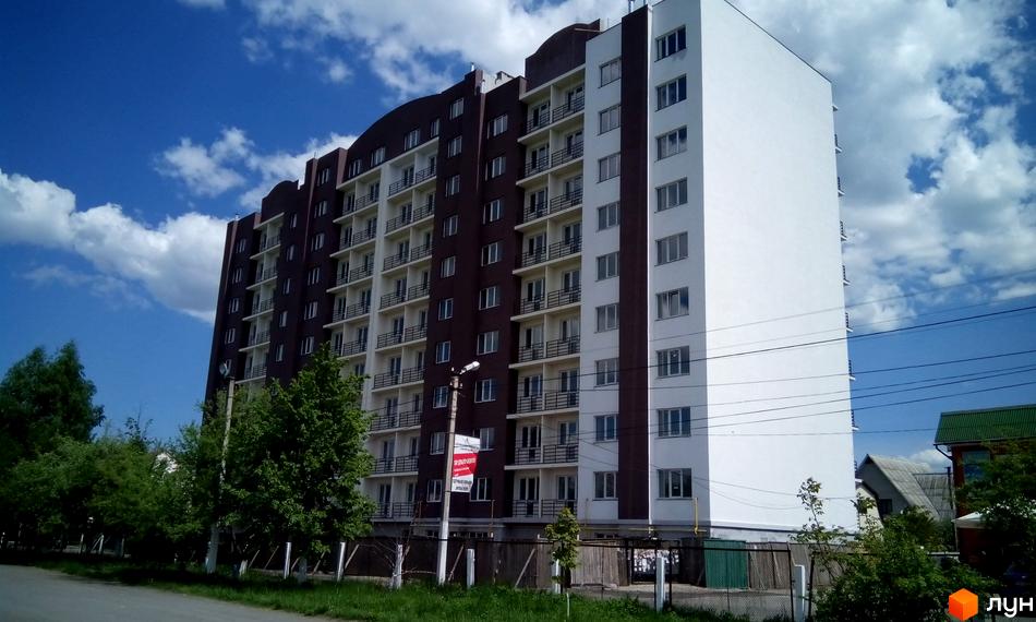 Житловий комплекс Вишнева оселя на вулиці Дружби. Багатоповерховий будинок з коричневою та білою частинами, балконами та вікнами.