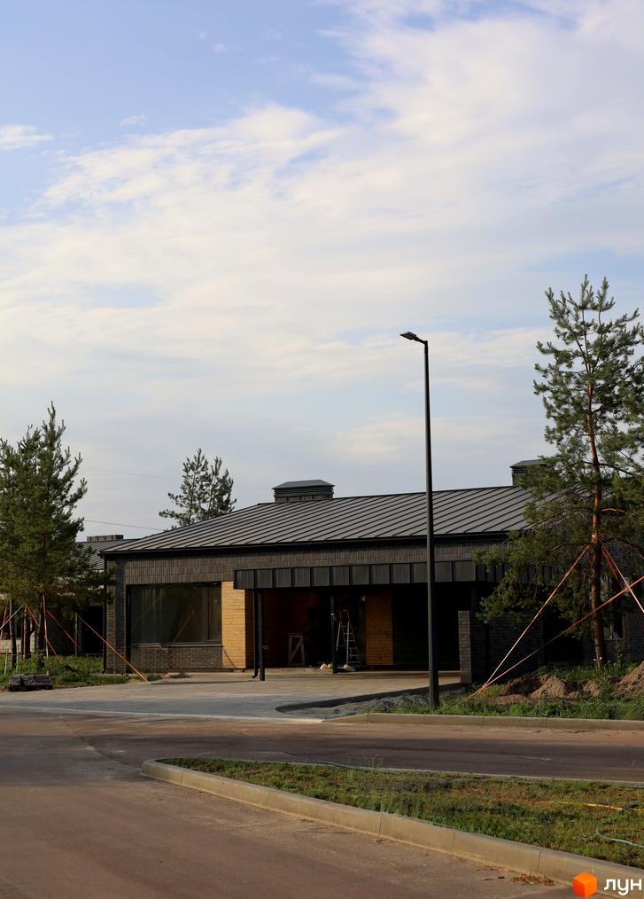 Котеджне містечко КМ NAVY Village з цегляним фасадом та великими вікнами, оточене соснами. Навколо будинку облаштована прибудинкова територія з доріжками та освітленням.