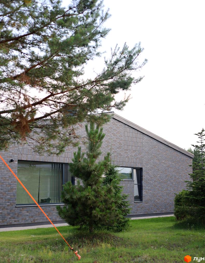 Котеджне містечко КМ NAVY Village з сірою цегляною стіною та зеленими деревами на прибудинковій території.