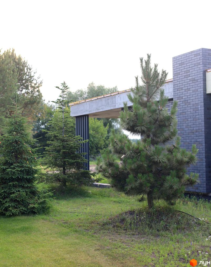 Зовнішній вигляд будинку КМ NAVY Village з цегляним фасадом та прибудинковою територією з деревами та газоном. Сучасна новобудова біля Києва.