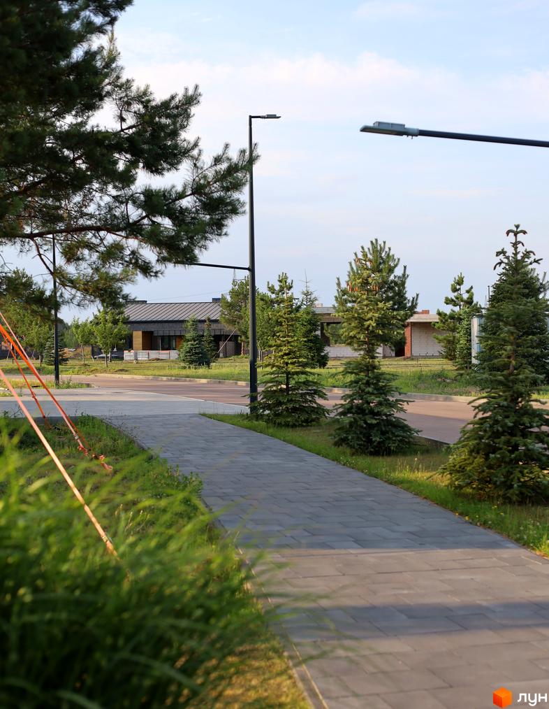 КМ NAVY Village: котеджне містечко з доглянутою прибудинковою територією, вимощеними доріжками та зеленими насадженнями. На фоні видно будинки з сучасними фасадами та металевими дахами.