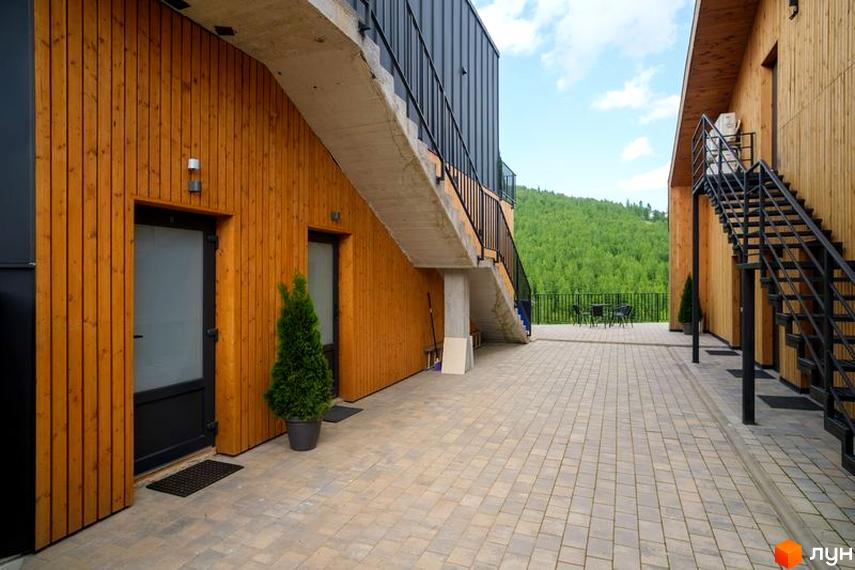 Апарт-готель Panorama Chalet з дерев'яним фасадом та зовнішніми сходами. Територія перед будинком вимощена плиткою, навколо зелені.