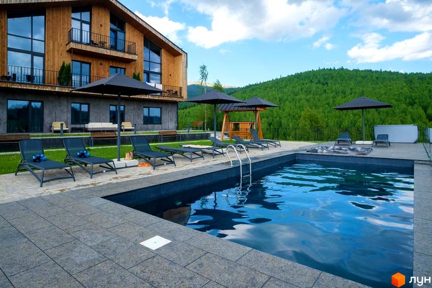 Апарт-готель Panorama Chalet з дерев'яним фасадом та великими вікнами, з басейном та шезлонгами на прибудинковій території.