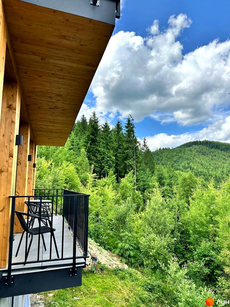 Апарт-готель Panorama Chalet: балкон з дерев'яною обшивкою та видом на зелені гори. На балконі розташовані столики та стільці.