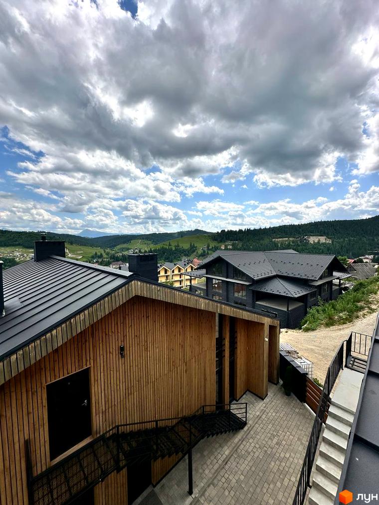Апарт-готель Panorama Chalet з дерев'яним фасадом та чорним дахом, розташований на схилі пагорба з видом на зелені гори.