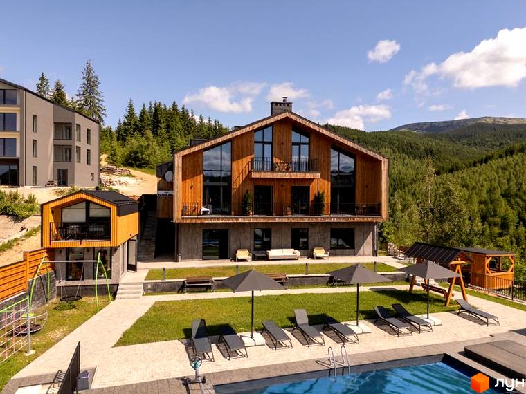 Апарт-готель Panorama Chalet з дерев'яним фасадом та великими вікнами, поруч басейн з шезлонгами та зелена зона.