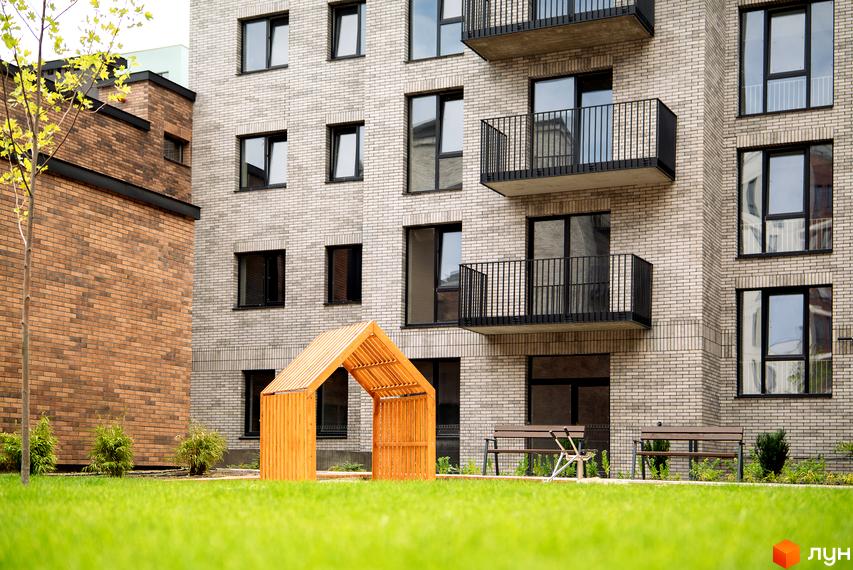 Будинок ЖК WAWEL з сірої цегли з балконами та прибудинкова територія з зеленим газоном та дерев'яною альтанкою.
