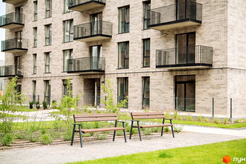 Новобудова ЖК WAWEL з цегляним фасадом та балконами. На прибудинковій території розташовані лавки та зелені насадження.