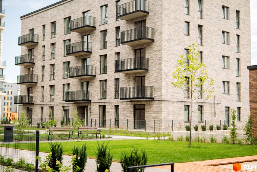 Будинок житлового комплексу WAWEL з цегляним фасадом та балконами. Поруч зелена галявина з лавками та деревами.