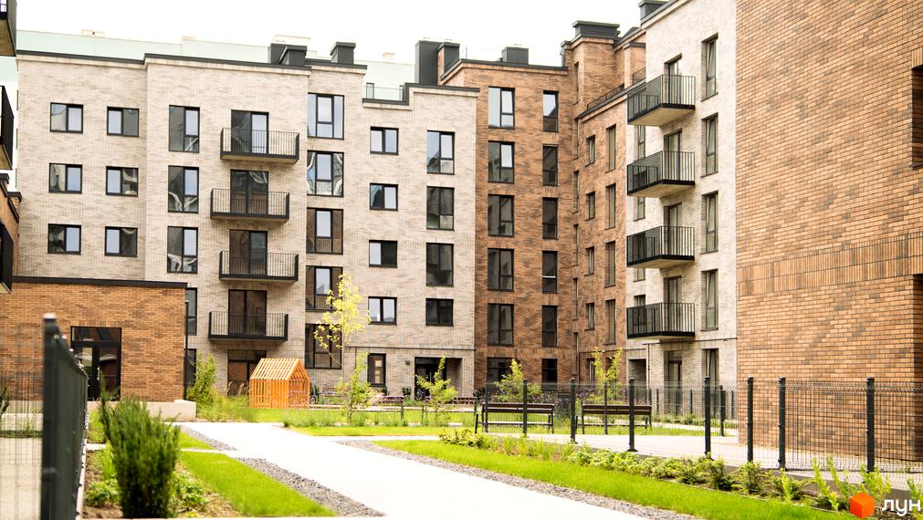 Зовнішній вигляд житлового комплексу WAWEL з цегляними фасадами та балконами. На прибудинковій території розташовані зелені зони та лавки.