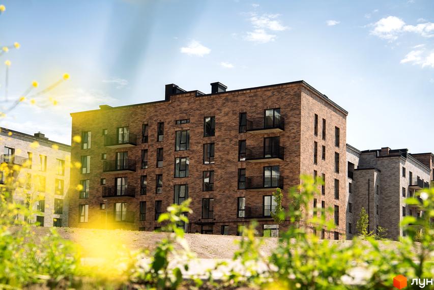 Новобудова WAWEL з цегляним фасадом та балконами на тлі блакитного неба. Навколо зелені насадження та квіти.