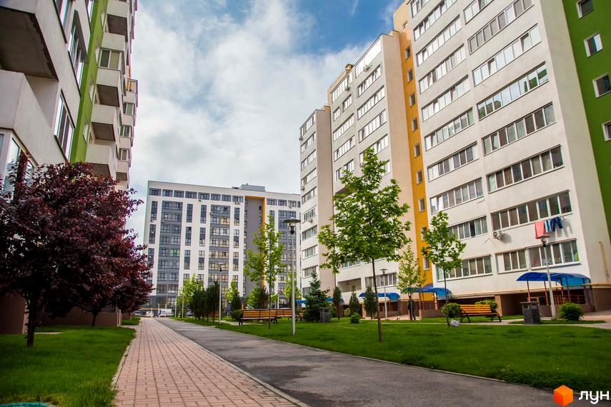 Житловий комплекс Піонерський квартал. Зовнішній вигляд багатоповерхових будинків з балконами та вікнами, зелена прибудинкова територія з деревами та лавками.