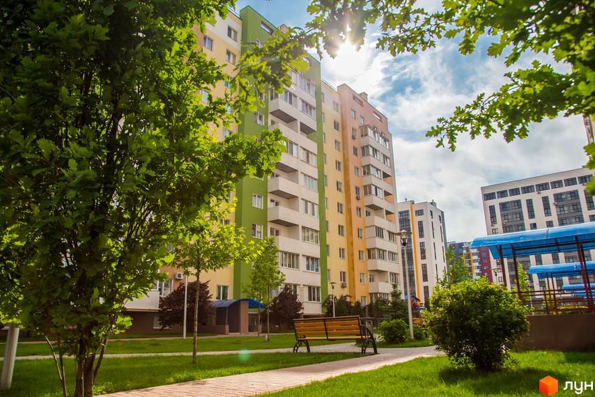 Житловий комплекс Піонерський квартал: багатоповерхові будинки з яскравими фасадами та зелена прибудинкова територія з лавкою та деревами.