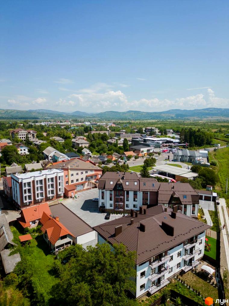 Новобудова ЖК Comfort House з коричневим дахом та білим фасадом, поруч зелена зона з дитячим майданчиком. Огляд комплексу з висоти пташиного польоту.
