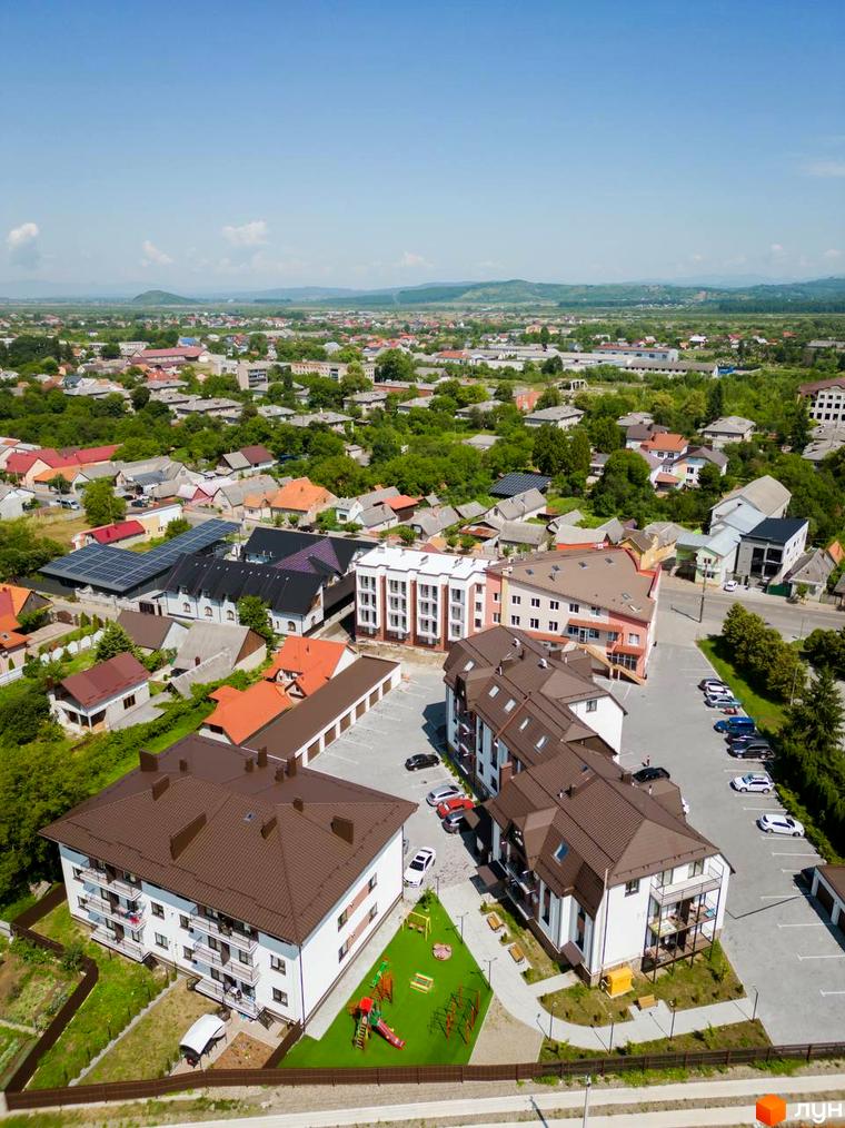 Житловий комплекс Comfort House з білими фасадами та коричневими дахами, поруч дитячий майданчик та парковка.