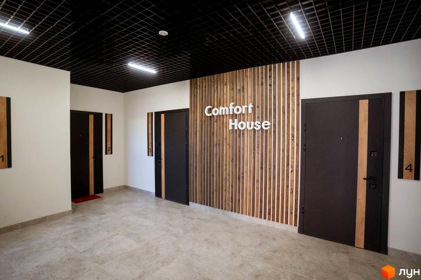 Вхідна група житлового комплексу Comfort House з дверима та номерами квартир. Сучасний дизайн холу з дерев'яною стіною та підвісною стелею.