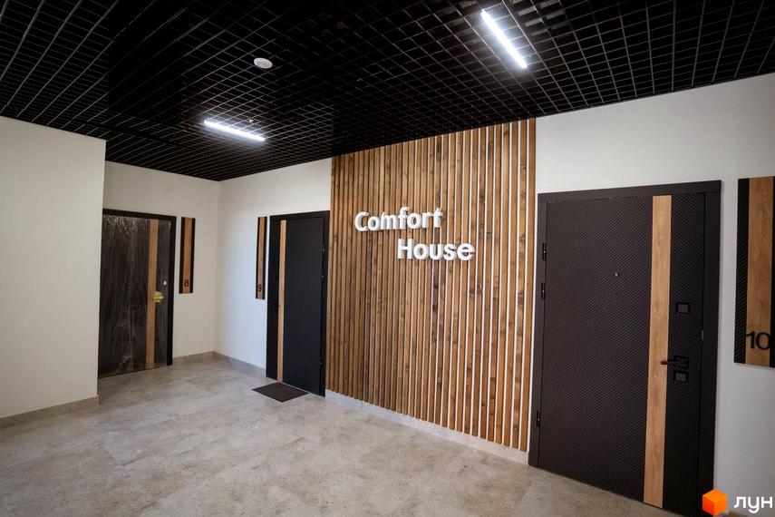 Вхідна група житлового комплексу Comfort House з дверима та декоративною стіною з дерев'яних рейок. На стіні розміщено назву комплексу.
