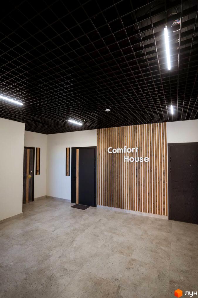 Вхідна група в житловий комплекс Comfort House з дверима та декоративною стіною з дерев'яних рейок. На стіні розміщено назву
