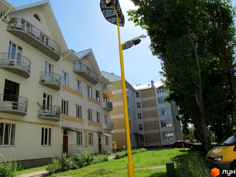 Зовнішній вигляд житлового комплексу Околиця з балконами та вікнами. Навколо будинку зелена територія з деревами та травою.