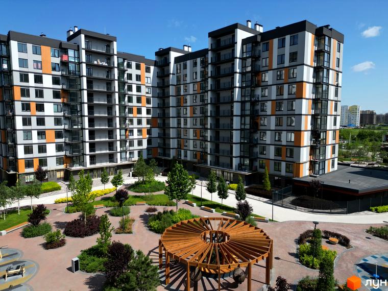 Житловий комплекс Атмосфера з сірими та помаранчевими фасадами, балконами та прибудинковою територією з ландшафтним дизайном та альтанкою.