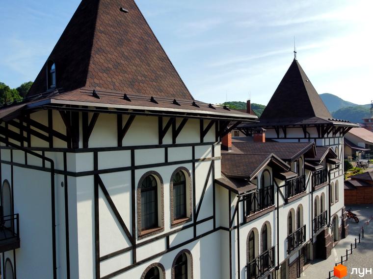 Житловий комплекс Shayan lux house з характерною архітектурою в стилі фахверк та коричневим черепичним дахом. Навколо будівлі видно зелені схили гір та елементи прибудинкової території.