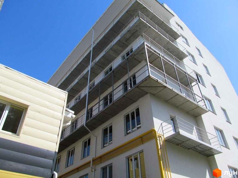 Зовнішній вигляд житлового комплексу Околиця з балконами та вікнами на фоні блакитного неба. Будівля має багатоповерхову структуру з відкритими балконами.