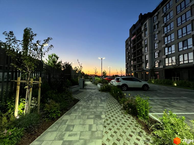 Житловий комплекс Park Residence з парковкою та доглянутою прибудинковою територією на заході сонця. Сучасна архітектура та зелені насадження створюють затишну атмосферу.