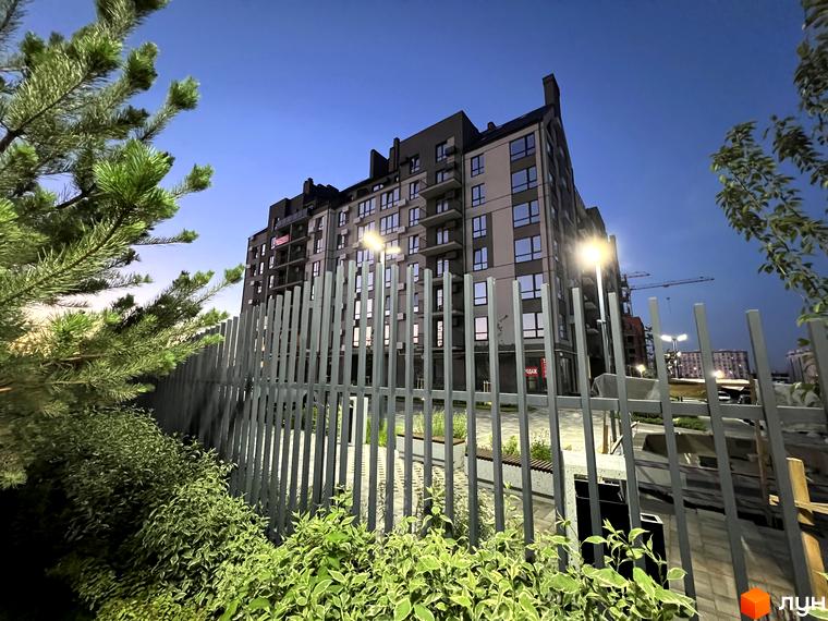 Житловий комплекс Park Residence з фасадом з сірих та бежевих панелей, вікнами та балконами, на фоні вечірнього неба. На прибудинковій території встановлено паркан та зелені насадження.