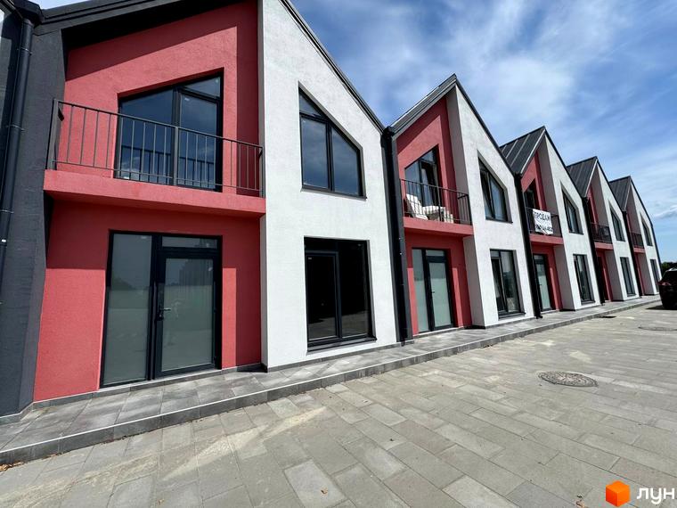 Таунхауси Freya – це двоповерхові будинки з червоними та білими фасадами, великими вікнами та балконами. Перед будинками розташована бруківка та сіра доріжка.
