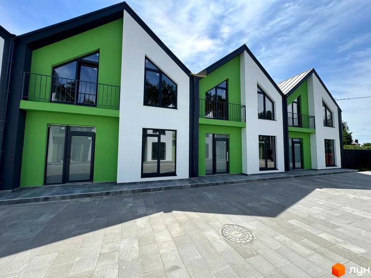 Таунхауси Freya - двоповерхові будинки з зеленими та білими фасадами, трикутними вікнами та балконами, розташовані на бруківці.