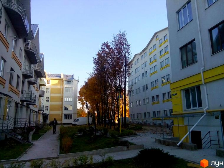 Житловий комплекс Околиця: фасади будинків з балконами та жовтими елементами, доглянута прибудинкова територія з деревами восени.