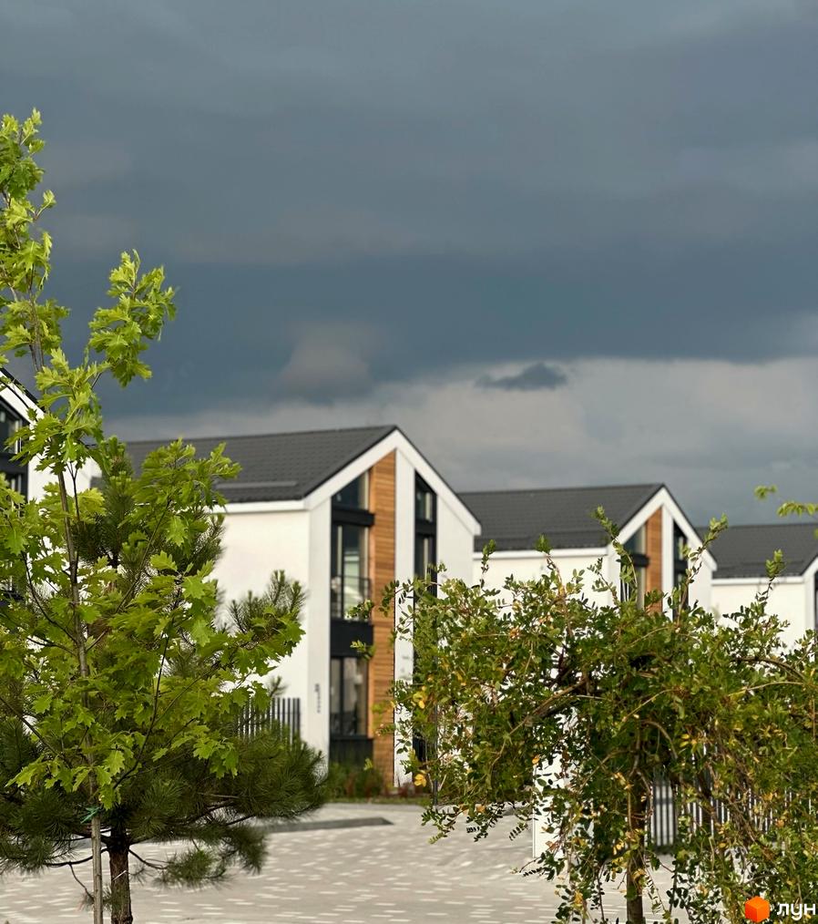 Котеджне містечко KМ Gardd House Eco Village: білі будинки з темними дахами та дерев'яними елементами, зелені дерева на території.