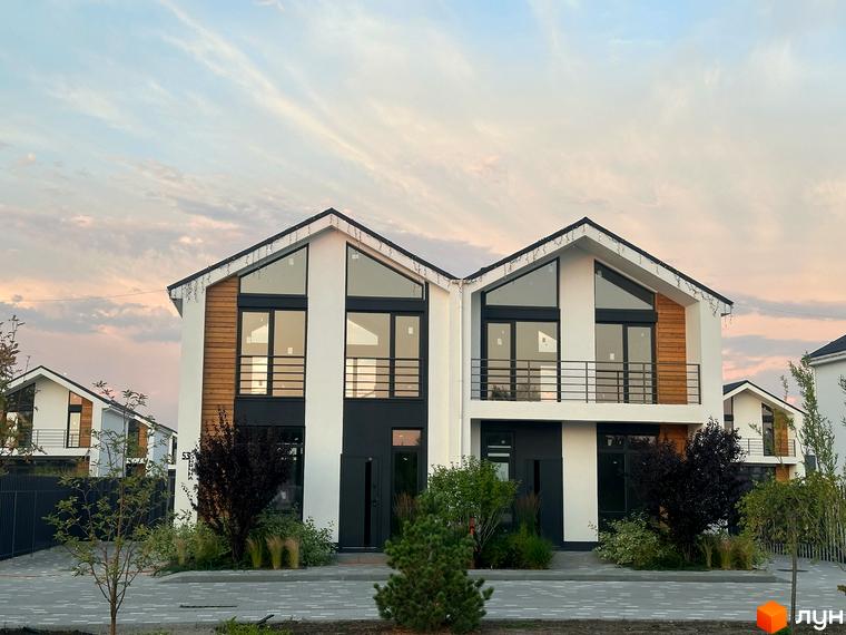 Котеджне містечко Gardd House Eco Village. Фасад будинку з великими вікнами та дерев'яними вставками, перед будинком зелені насадження та бруківка.