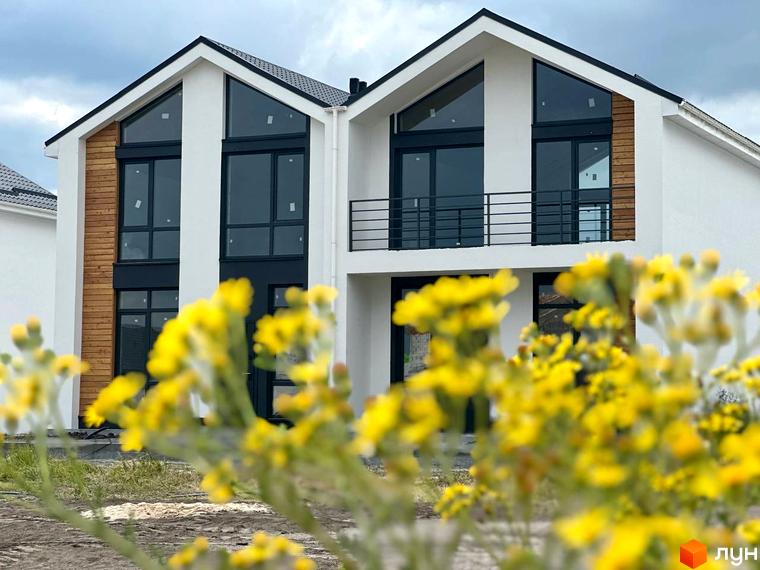 Котеджне містечко Gardd House Eco Village. Фасад будинку з великими вікнами та дерев'яними елементами, перед будинком жовті квіти.