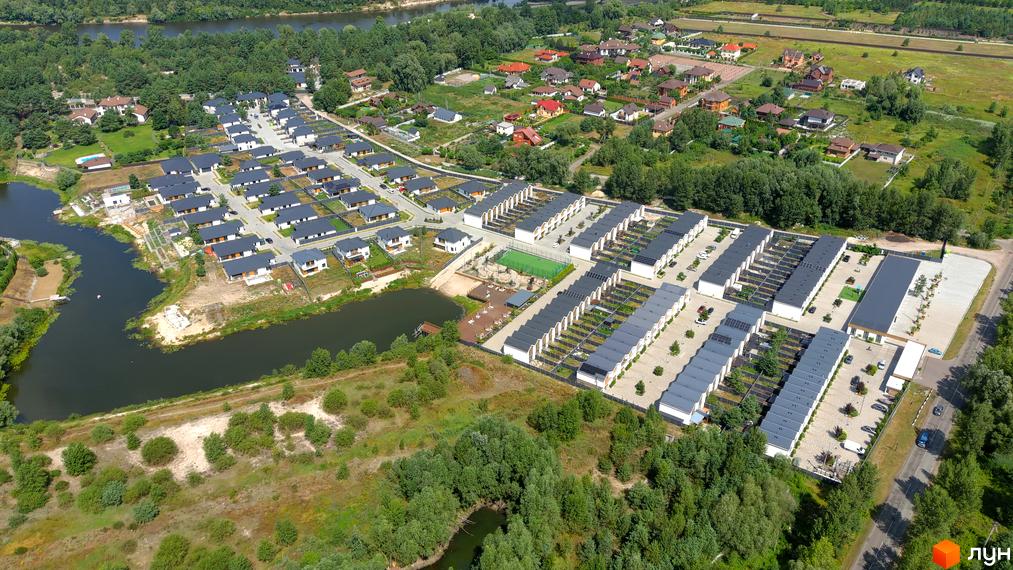 Котеджне містечко Prydesennya Eco Village з сучасними будинками та доглянутою прибудинковою територією, що включає зелені зони та водойму.