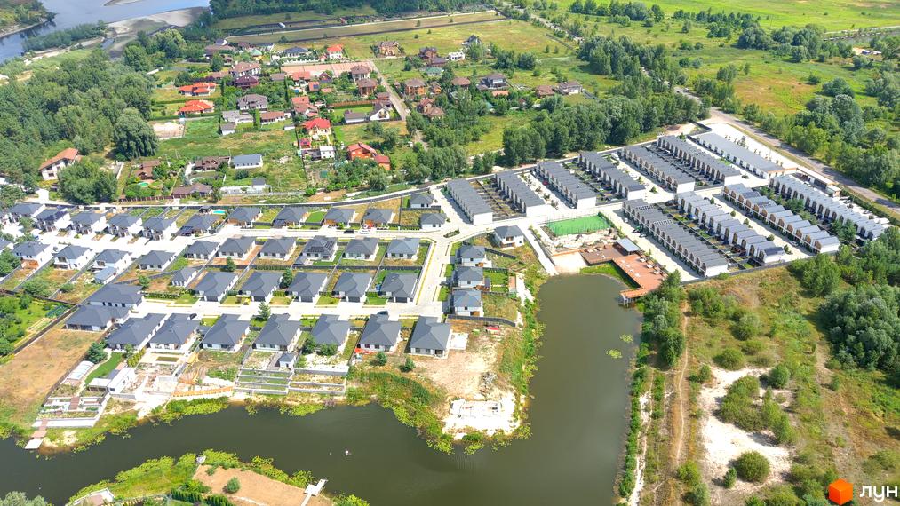 Котеджне містечко КМ Prydesennya Eco Village з сучасними будинками та доглянутою прибудинковою територією біля озера. На фото видно ряди будинків з сірими дахами та зелені зони.