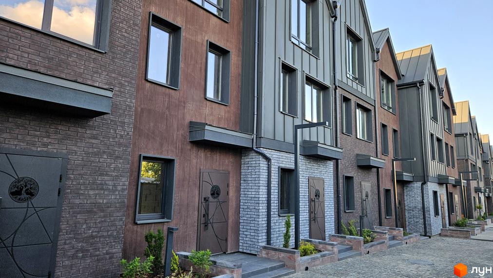 Зовнішній вигляд таунхаусів New Smart 17 з цегляним та дерев'яним фасадом, вікнами та дверима з кованими елементами. Прибудинкова територія з бруківкою та зеленими насадженнями.