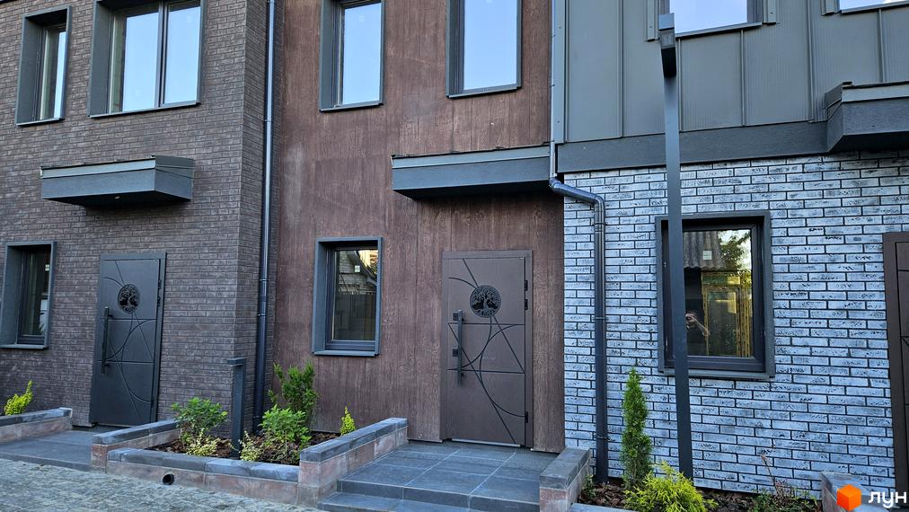Фасад таунхаусів New Smart 17 з цегляним оздобленням та дерев'яними елементами, перед будинком облаштована прибудинкова територія з рослинами.