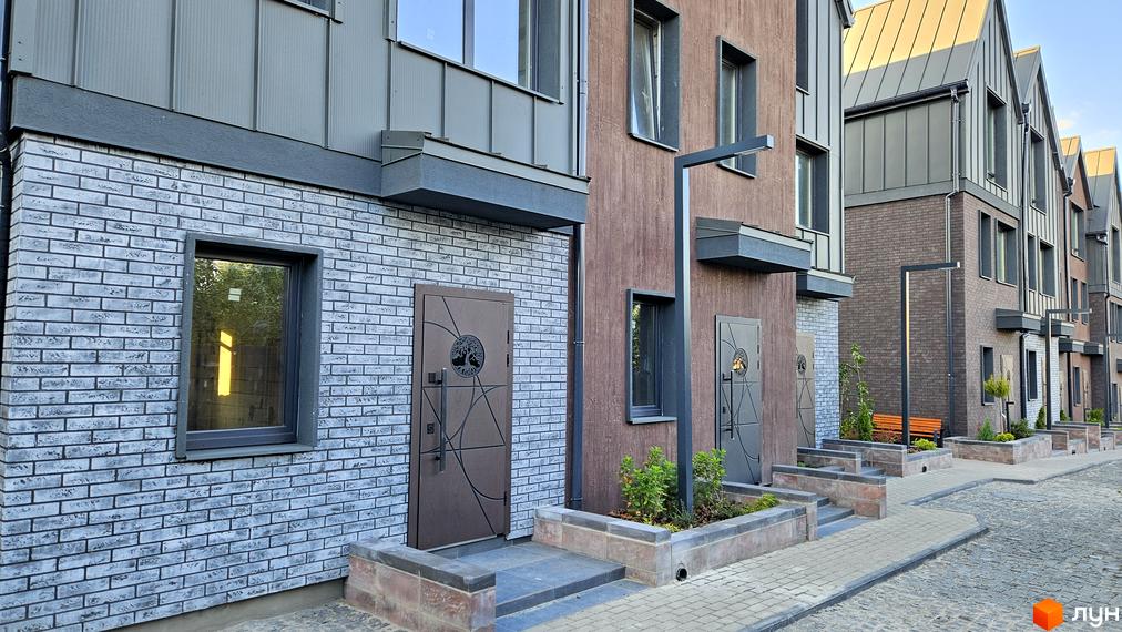 Таунхауси New Smart 17 з цегляним фасадом та дерев'яними елементами, розташовані вздовж бруківки з лавками та зеленню.