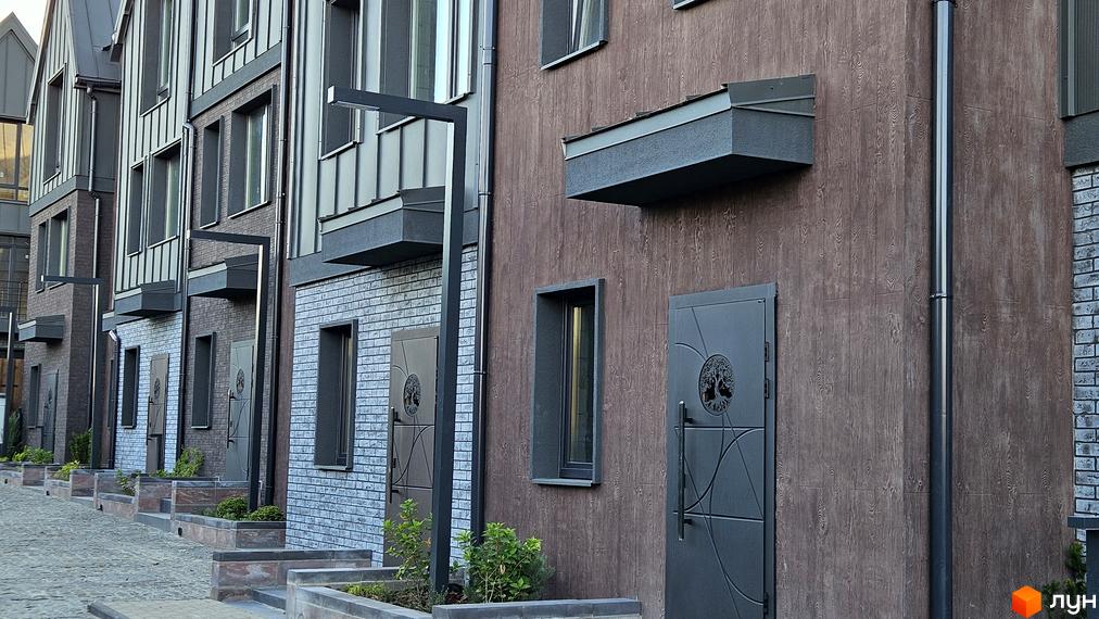 Фасад таунхаусів New Smart 17 з цегляним оздобленням та дерев'яними панелями. Поруч розташовані клумби з рослинами та вимощена бруківкою доріжка.