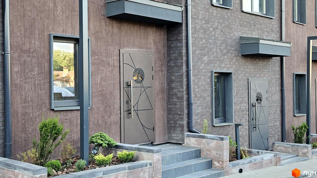 Таунхауси New Smart 17: фасади з дерев'яною обшивкою та цегляною кладкою, вхідні групи з дверима та вікнами, облаштована прибудинкова територія з рослинністю.