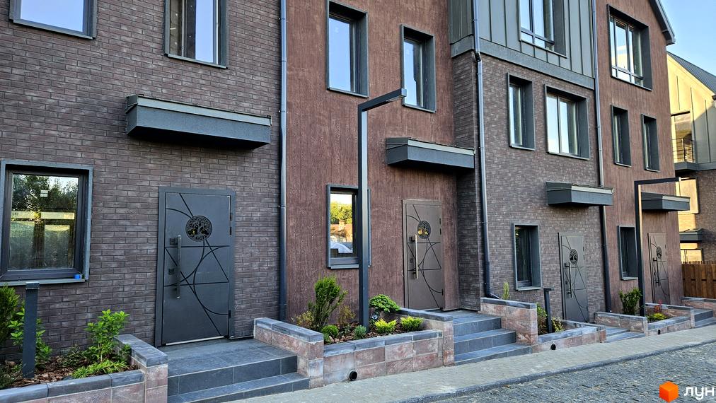 Фасад таунхаусів New Smart 17 з цегляним оздобленням та дерев'яними елементами. Прибудинкова територія з квітниками та бруківкою.