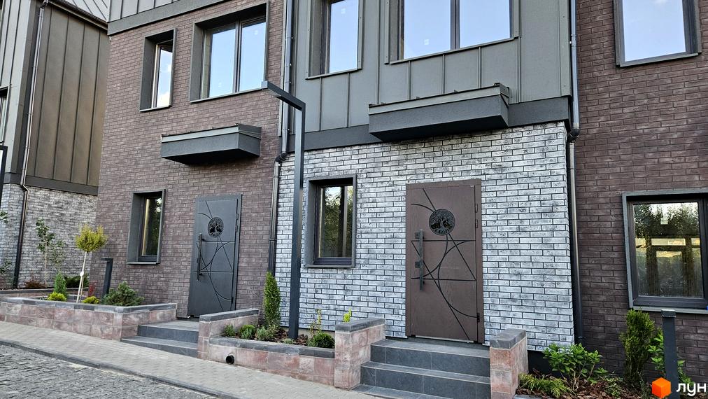 Таунхауси New Smart 17: фасади з цегли та металевих панелей, вхідні групи з декоративними дверима, перед будинками облаштовані клумби та сходи.