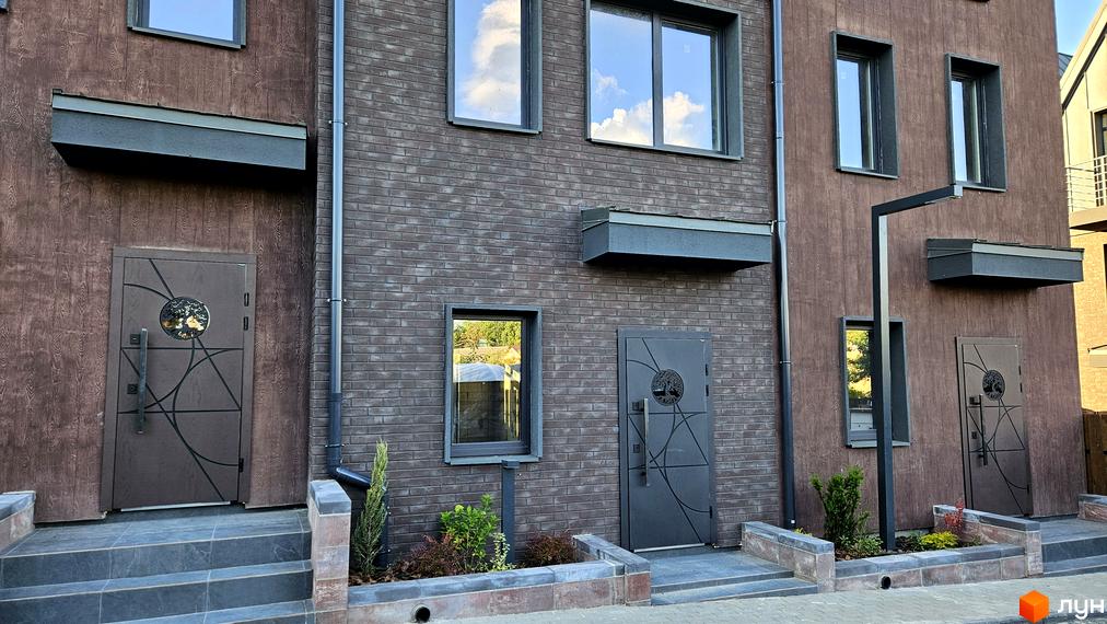 Зовнішній вигляд таунхаусів New Smart 17 з цегляним фасадом та дерев'яними елементами. Прибудинкова територія з доглянутими клумбами та сходами.