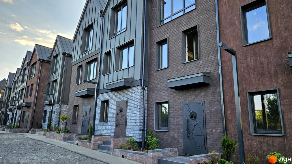 Зовнішній вигляд таунхаусів New Smart 17 з цегляним фасадом та металевим дахом. Прибудинкова територія з бруківкою та зеленими насадженнями.