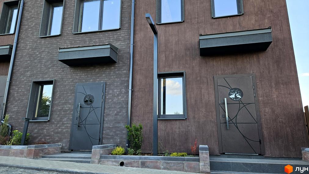 Таунхауси New Smart 17: фасади з цегляним та дерев'яним оздобленням, вхідні групи з дверима, вікнами та ліхтарем. Прибудинкова територія з рослинами та бруківкою.