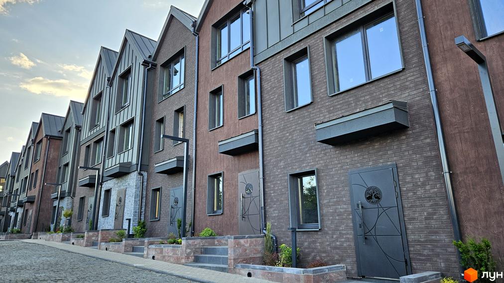 Зовнішній вигляд таунхаусів New Smart 17 з цегляним фасадом та темним дахом. Прибудинкова територія з бруківкою та зеленими насадженнями.