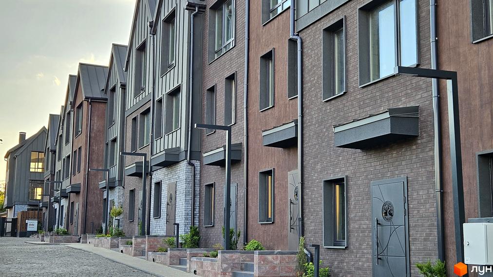 Таунхауси New Smart 17 – це сучасна новобудова з цегляним фасадом та металевим дахом, розташована на бруківці з доглянутими клумбами.